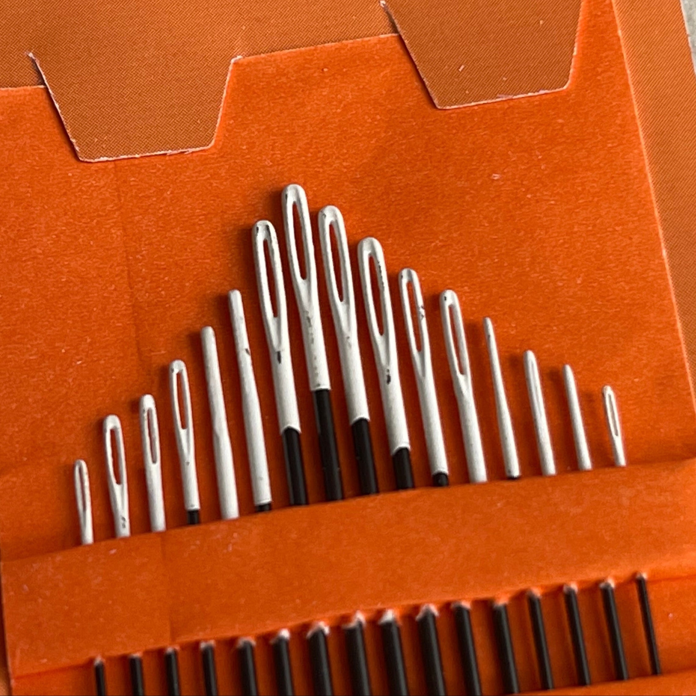 Set of metal needles in an orange holder with a white background