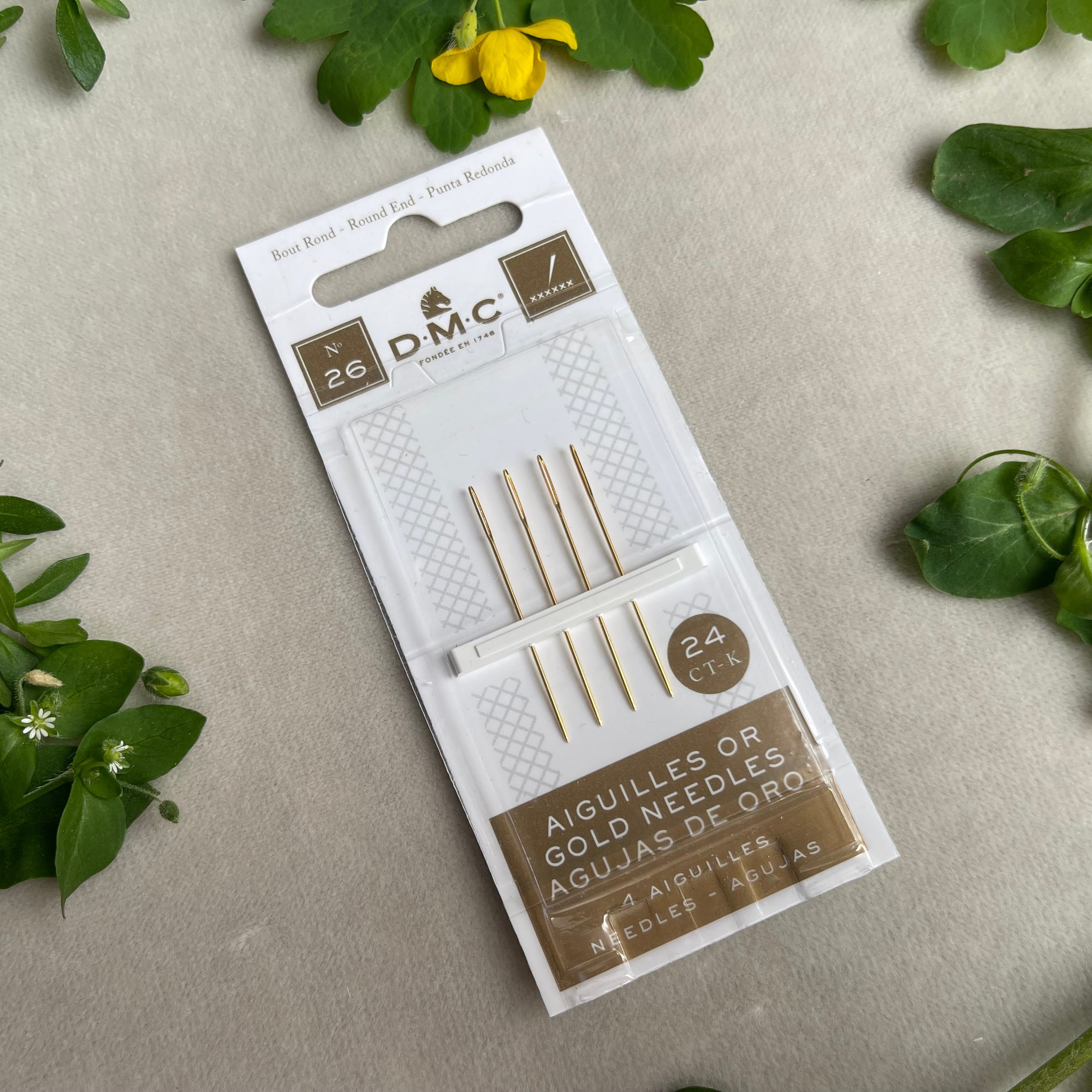 DMC needle packet on a gray surface with green leaves