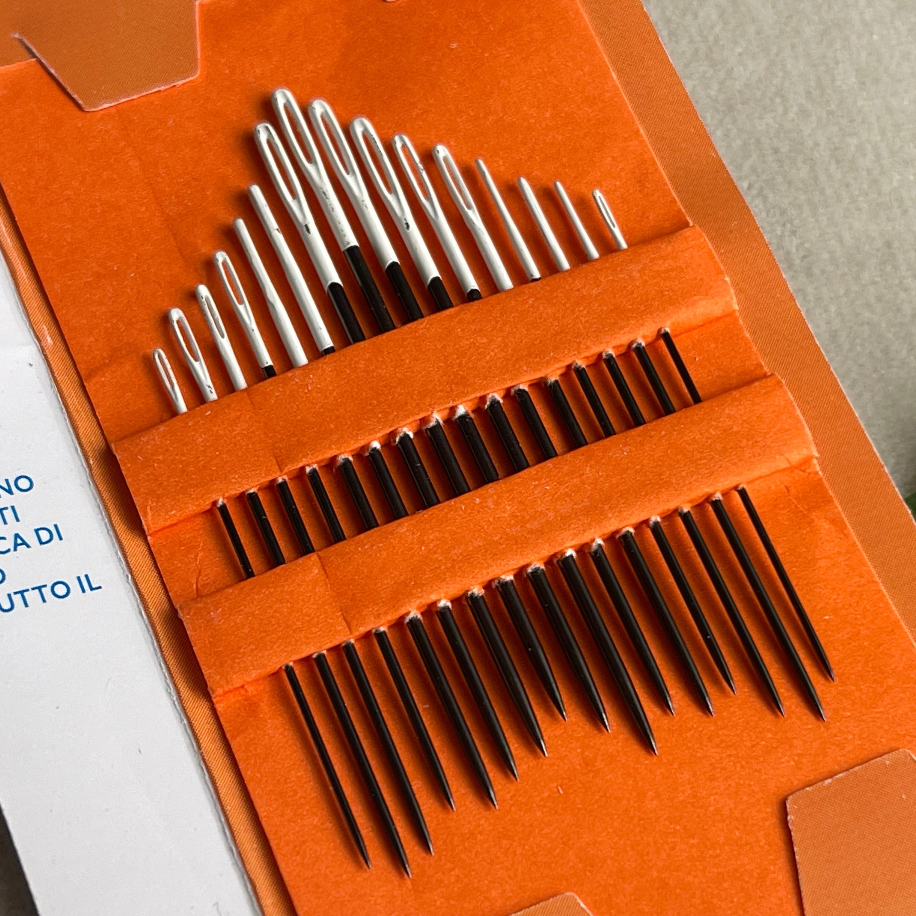 Set of metal needles in an orange case on a gray surface with text in the background.