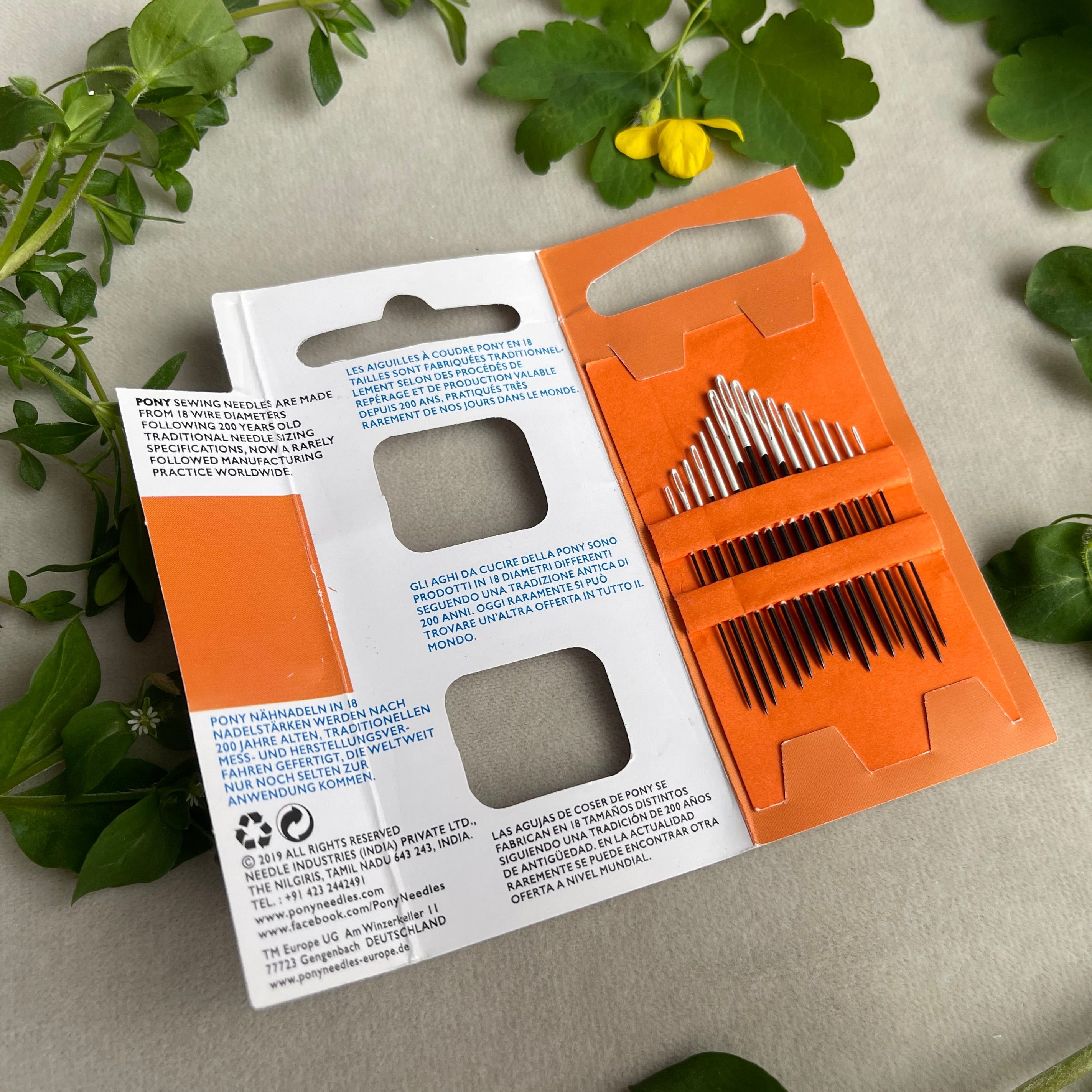 Orange and white packaging of needles on a light gray background with green leaves.