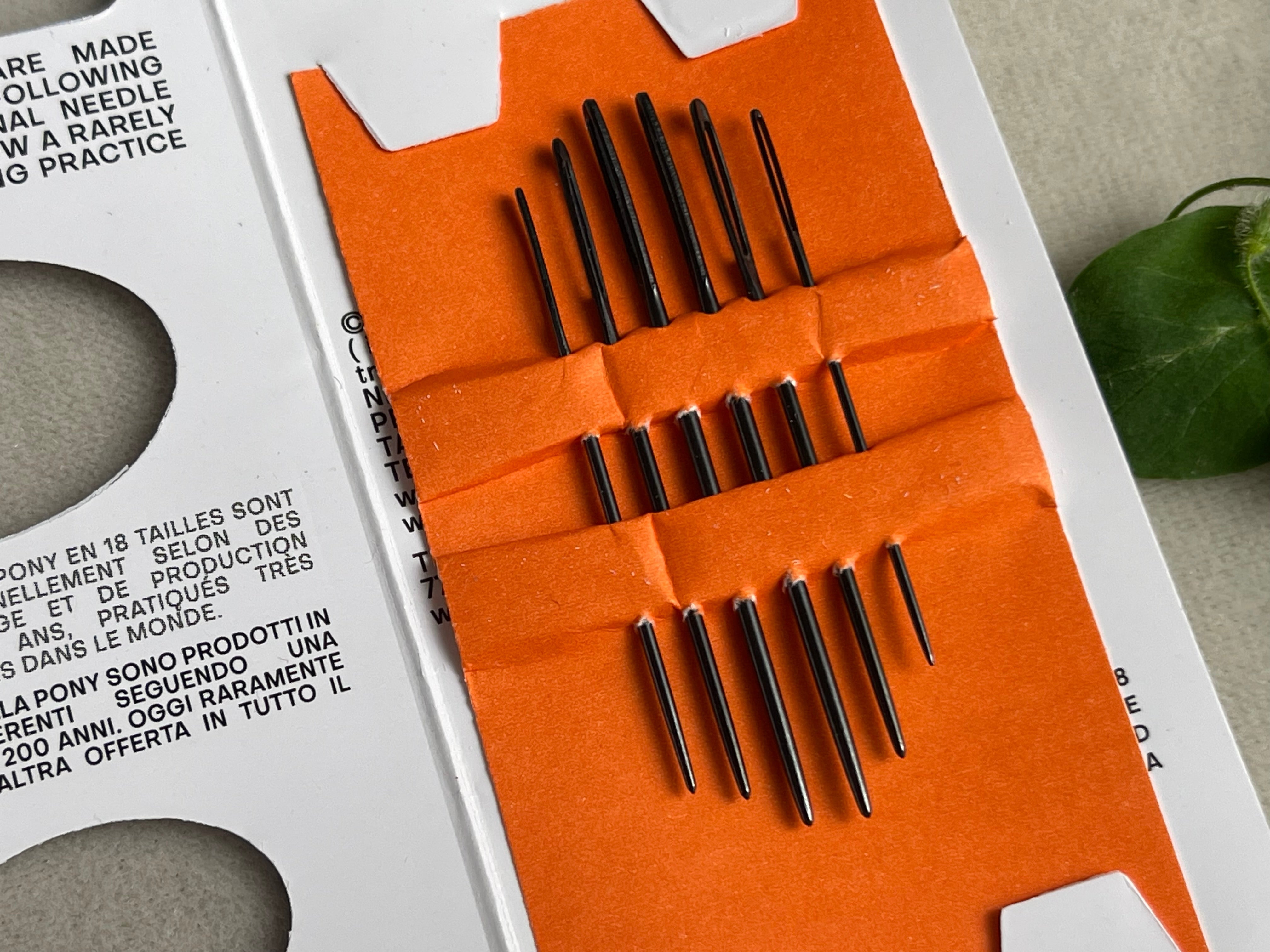 Set of black needles in an orange holder on a white background with text.
