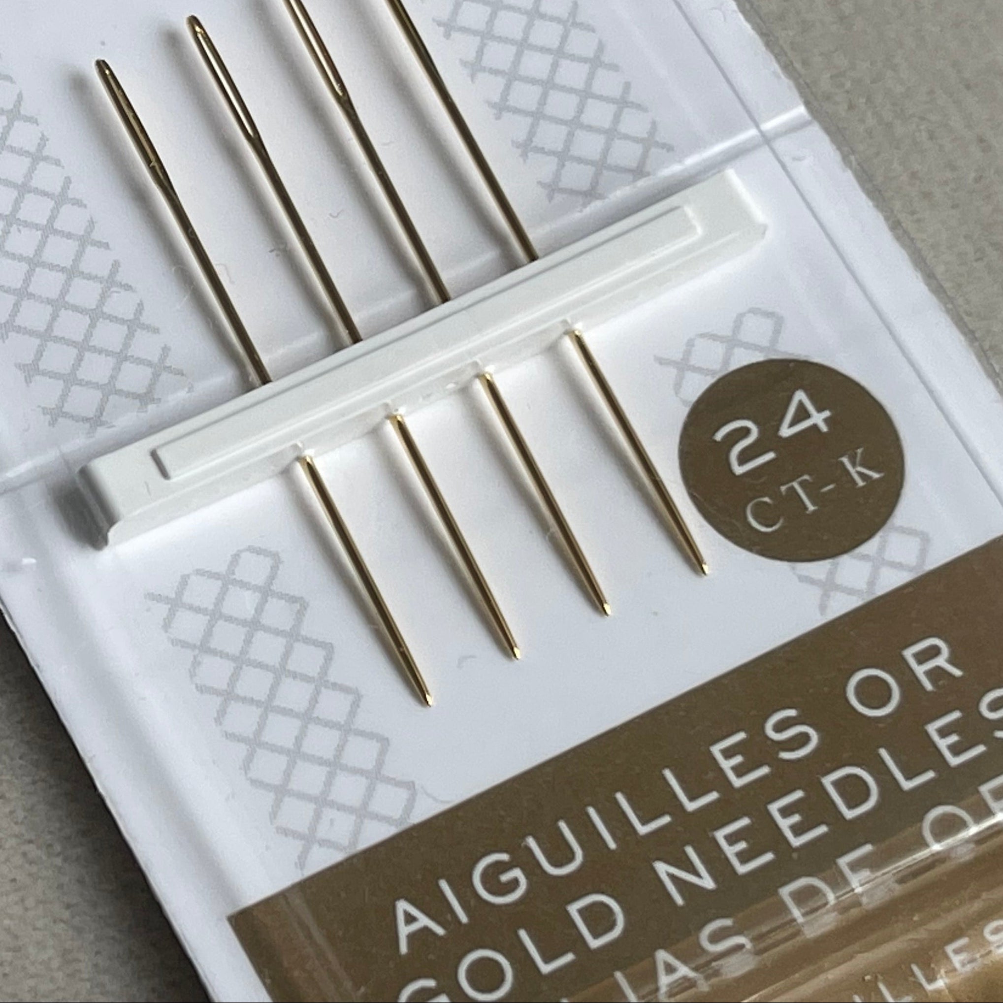 Packaged gold embroidery needles with DMC branding on a gray background
